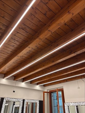 Soffitto in legno con travi a vista e luci a neon sopra una stanza luminosa con finestre e una porta