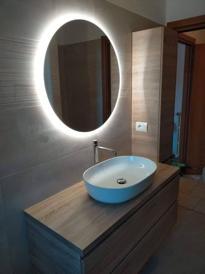 Mobile bagno moderno con specchio ovale illuminato e lavabo a ciotola blu.