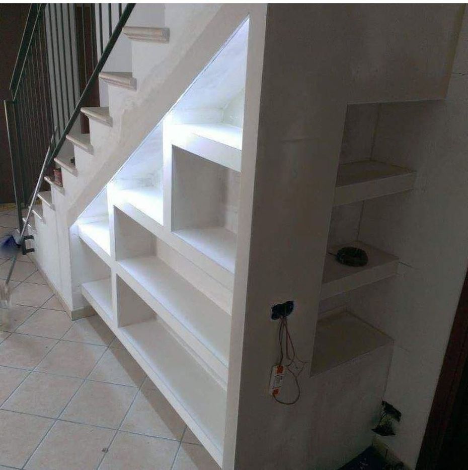 Scaffalature bianche a muro sotto una scala in un corridoio interno piastrellato.