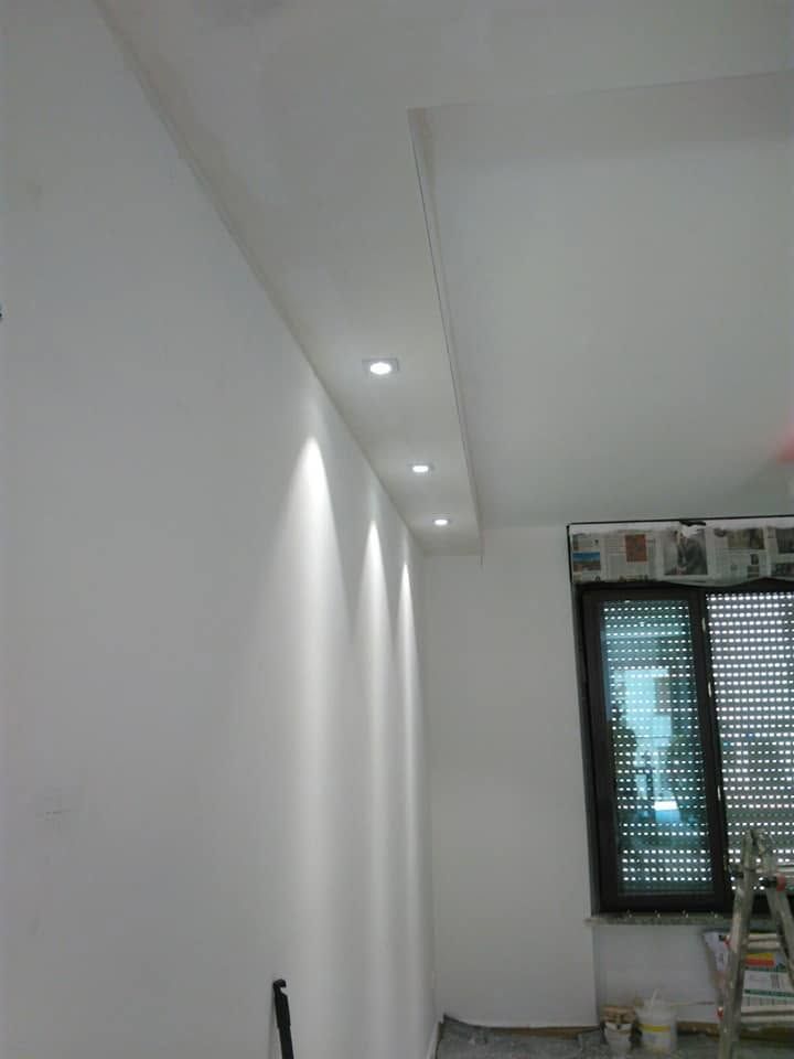 Corridoio bianco con faretti a incasso sul soffitto e una finestra in fondo.