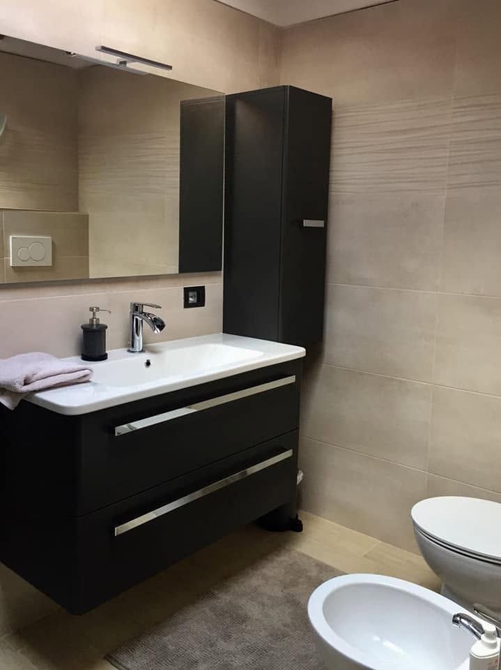 Bagno moderno con mobiletto nero, lavabo e WC bianchi, pareti piastrellate beige e specchio con armadietto.