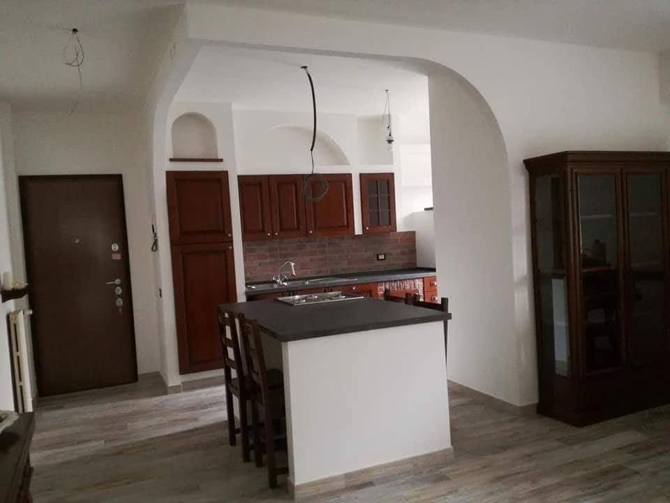 Cucina di piccole dimensioni con isola centrale, mobili in legno scuro e una porta che conduce a un'altra stanza.