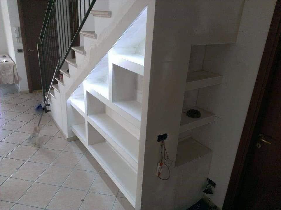 Scala bianca con scaffalature integrate in un corridoio interno piastrellato.