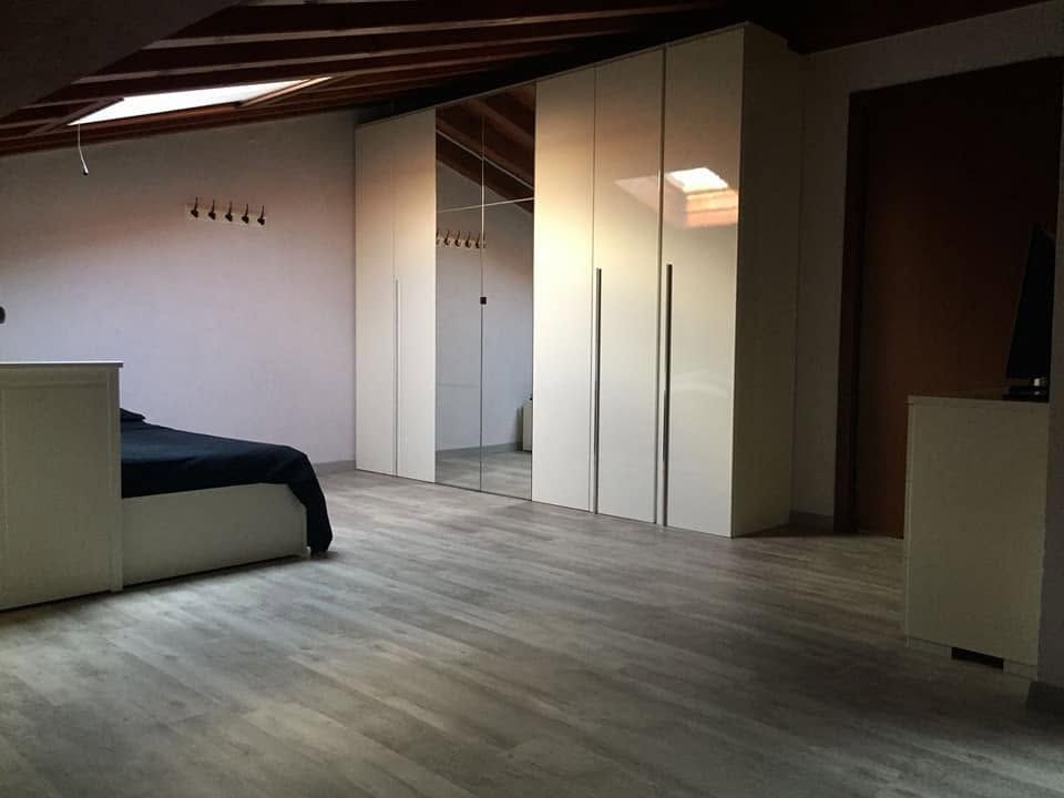 Camera da letto minimalista in mansarda con soffitto in legno inclinato, letto, armadio con specchio e scrivania.