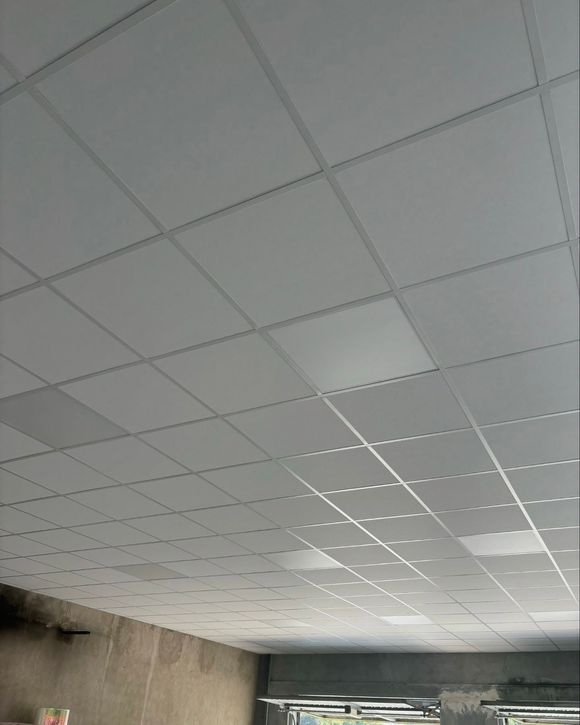 Soffitto interno con pannelli acustici bianchi e luci fluorescenti sopra pareti in cemento grezzo