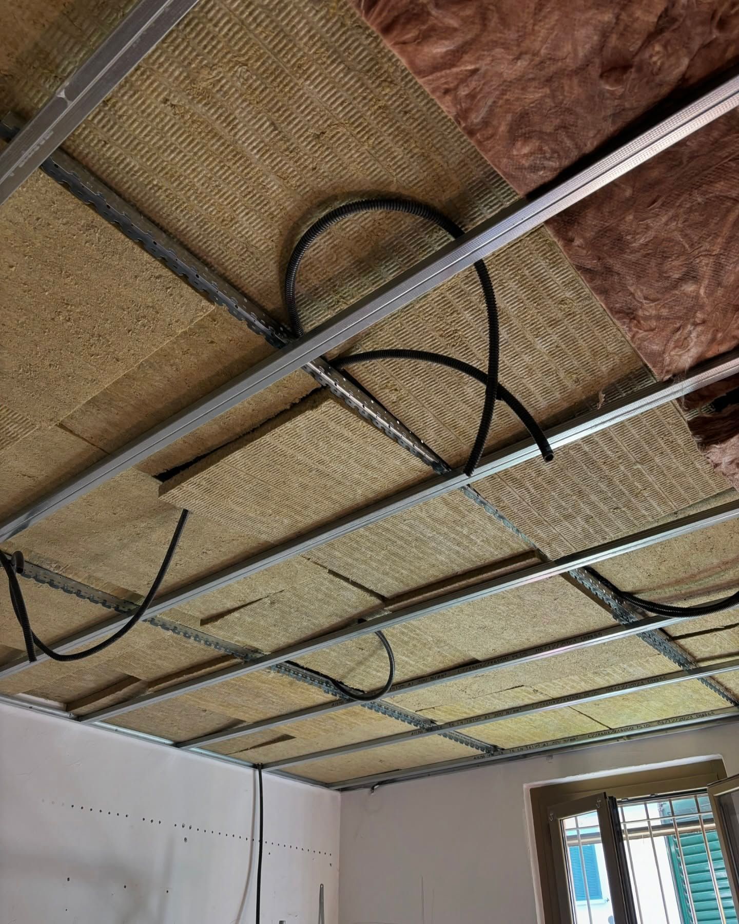 Soffitto in costruzione con pannelli isolanti, cavi a vista e struttura metallica.