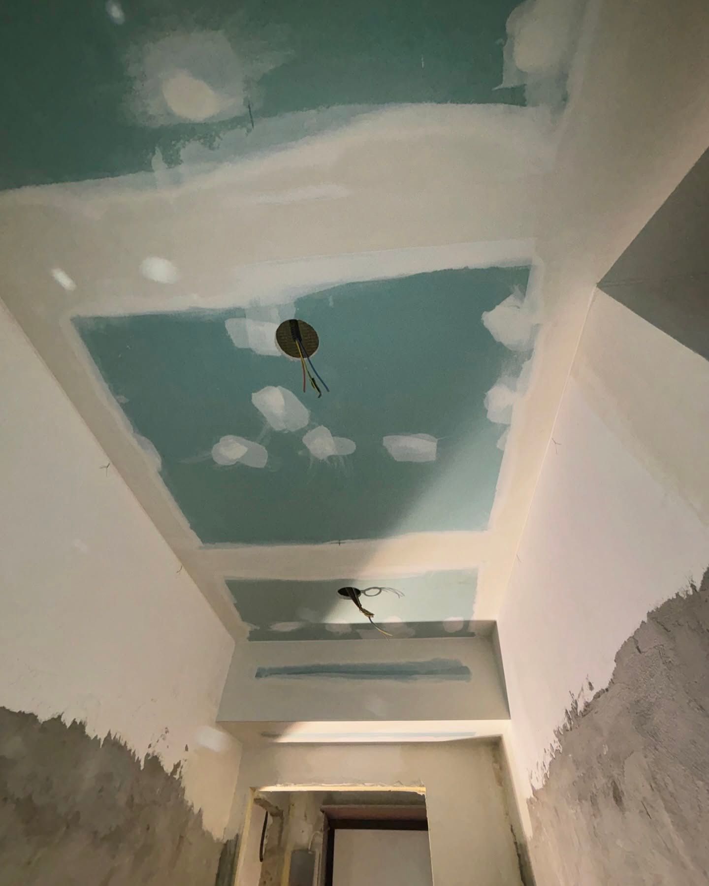 Soffitto del corridoio parzialmente rifinito con rattoppi di cartongesso e apparecchi di illuminazione a vista.
