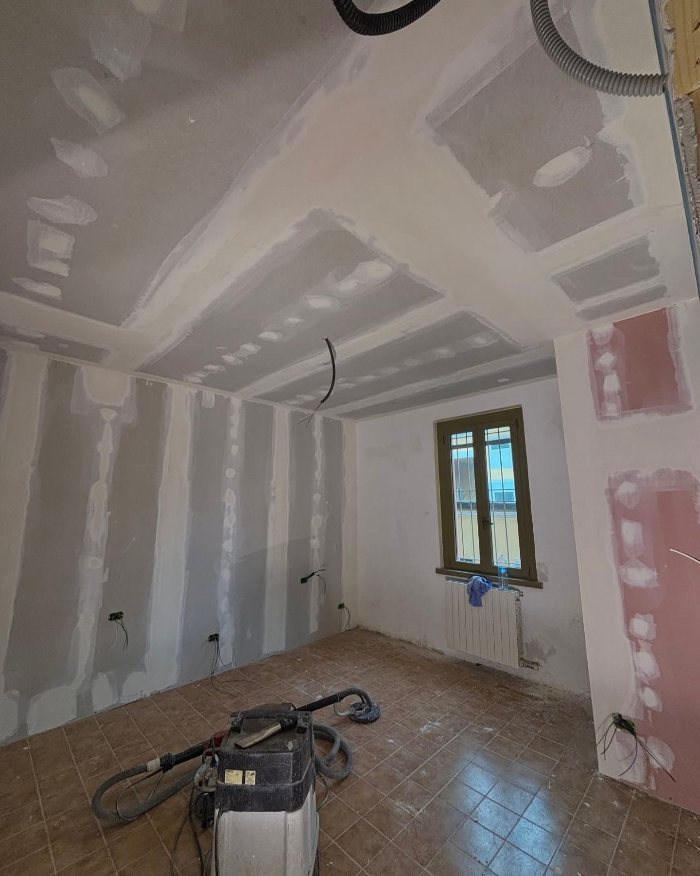 Stanza parzialmente finita con riparazioni al muro a secco, una finestra e attrezzi sul pavimento.
