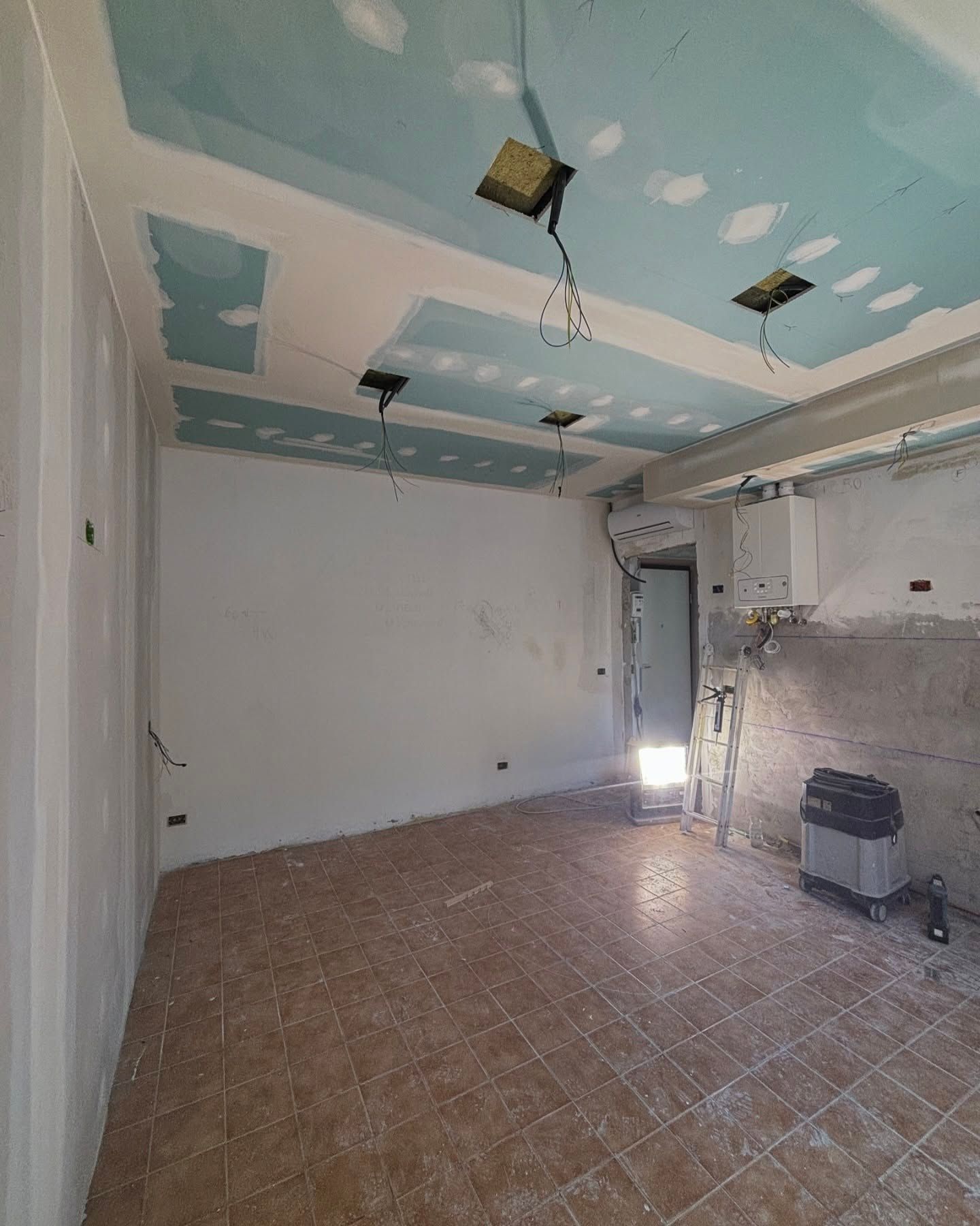 Stanza vuota in fase di ristrutturazione con soffitto blu, pareti bianche e pavimento piastrellato.