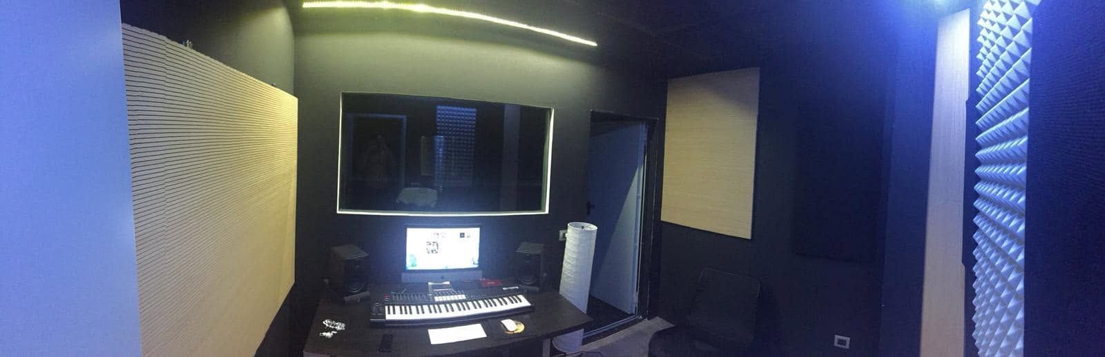 Piccolo studio di registrazione con scrivania, monitor, altoparlanti e illuminazione a LED blu-viola.