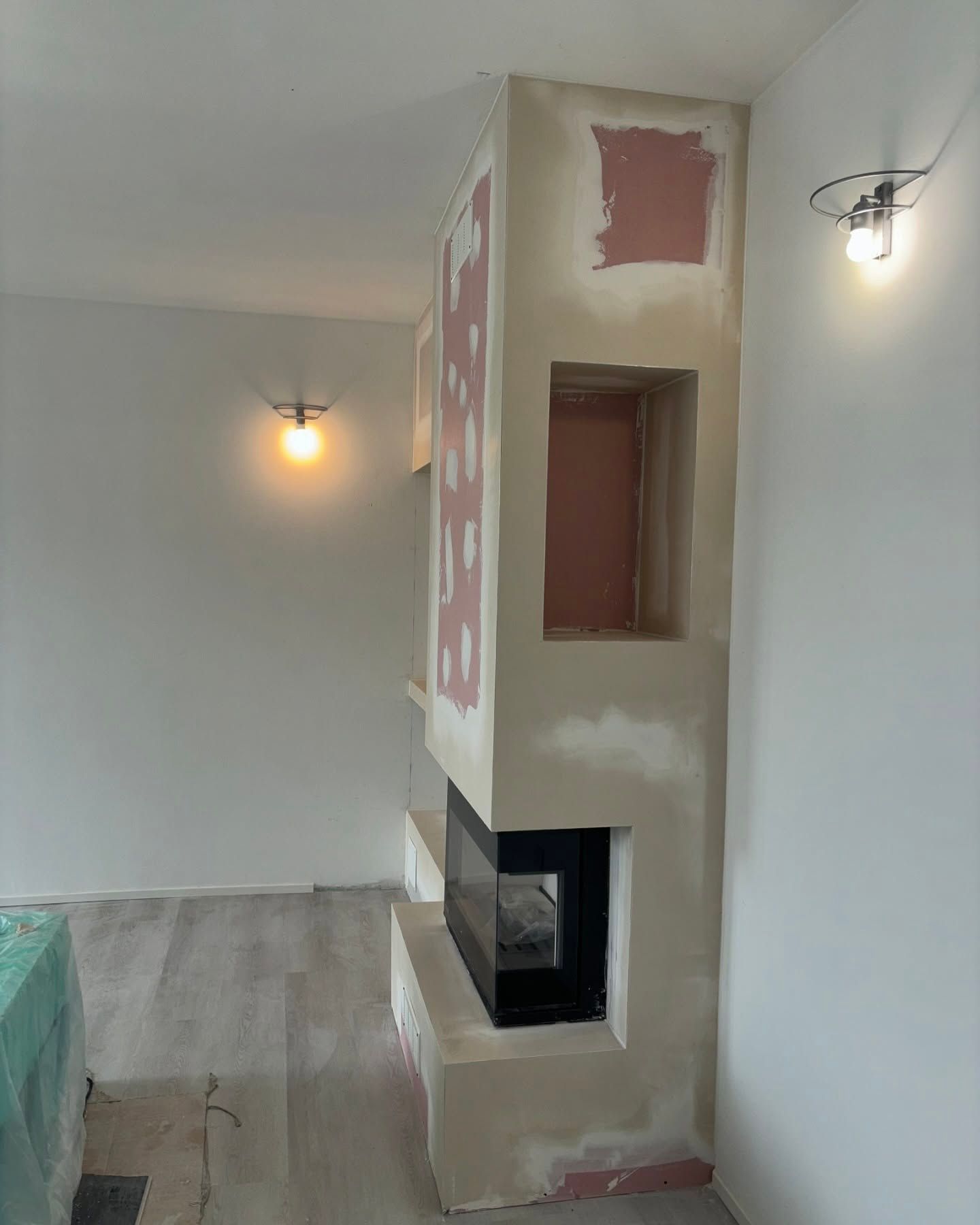 Soggiorno con camino o stufa a incasso beige accanto a una parete bianca e pavimento in legno.
