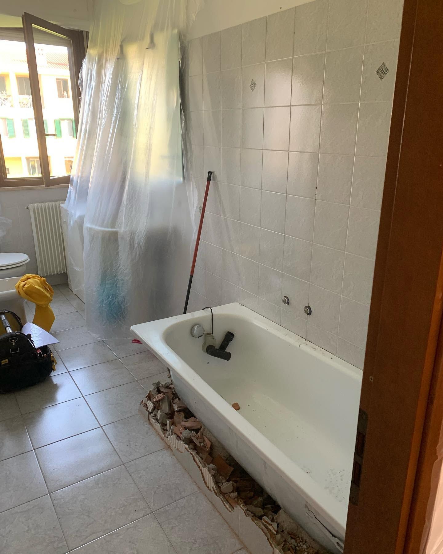 Piccolo bagno con vasca, pareti piastrellate e finestra coperta da una tenda trasparente.