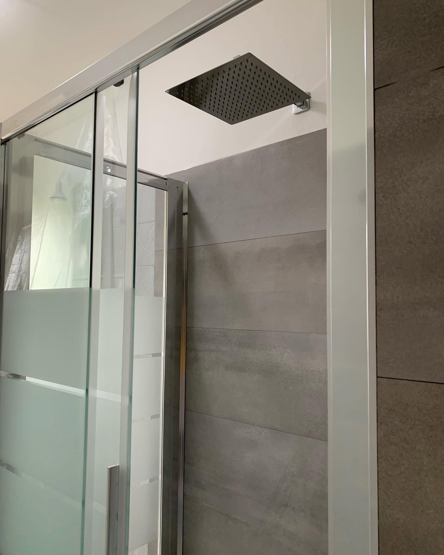 Box doccia in vetro con pannelli inferiori satinati e soffione a pioggia quadrato a parete.