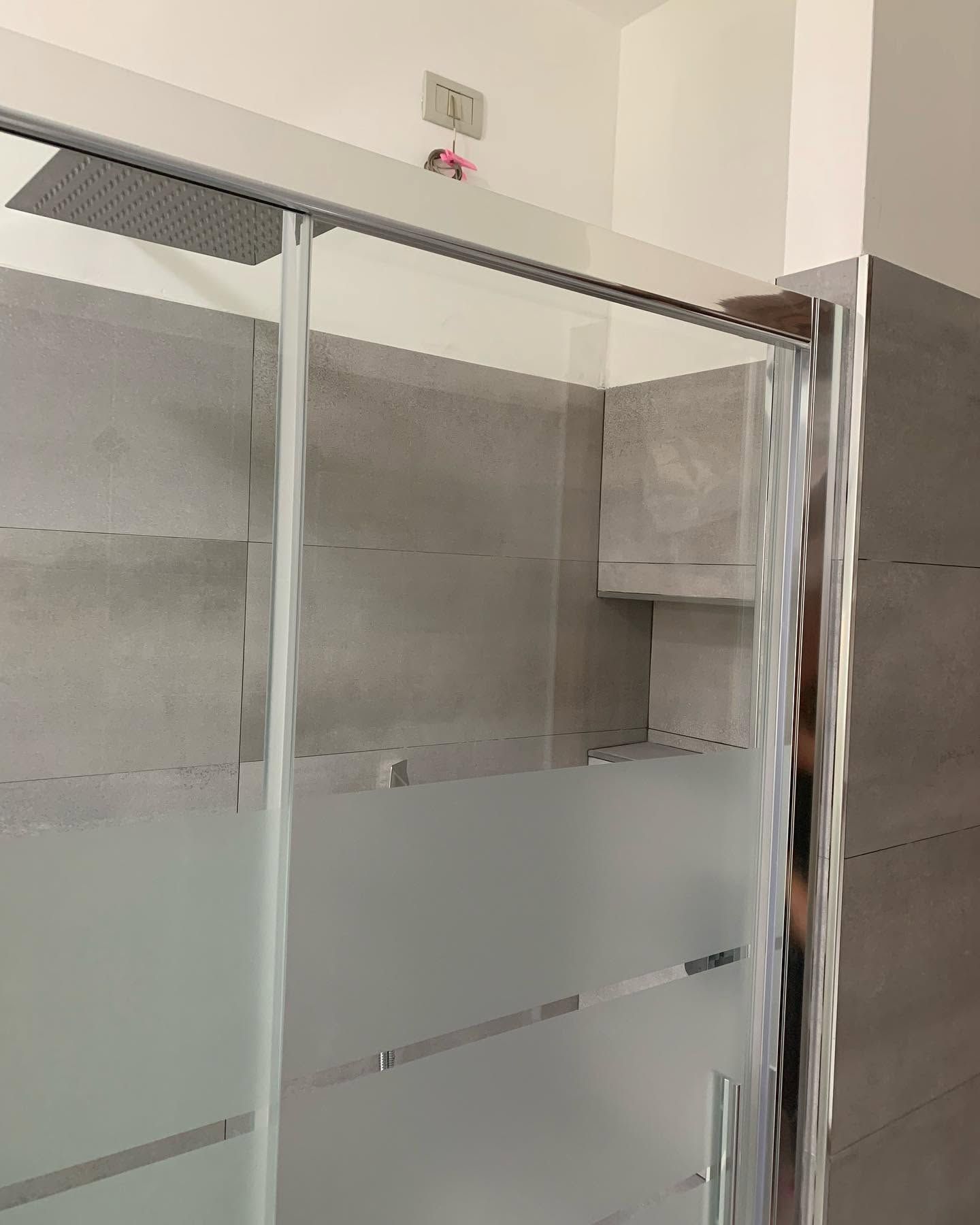 Box doccia in vetro satinato con telaio cromato in un bagno piastrellato.