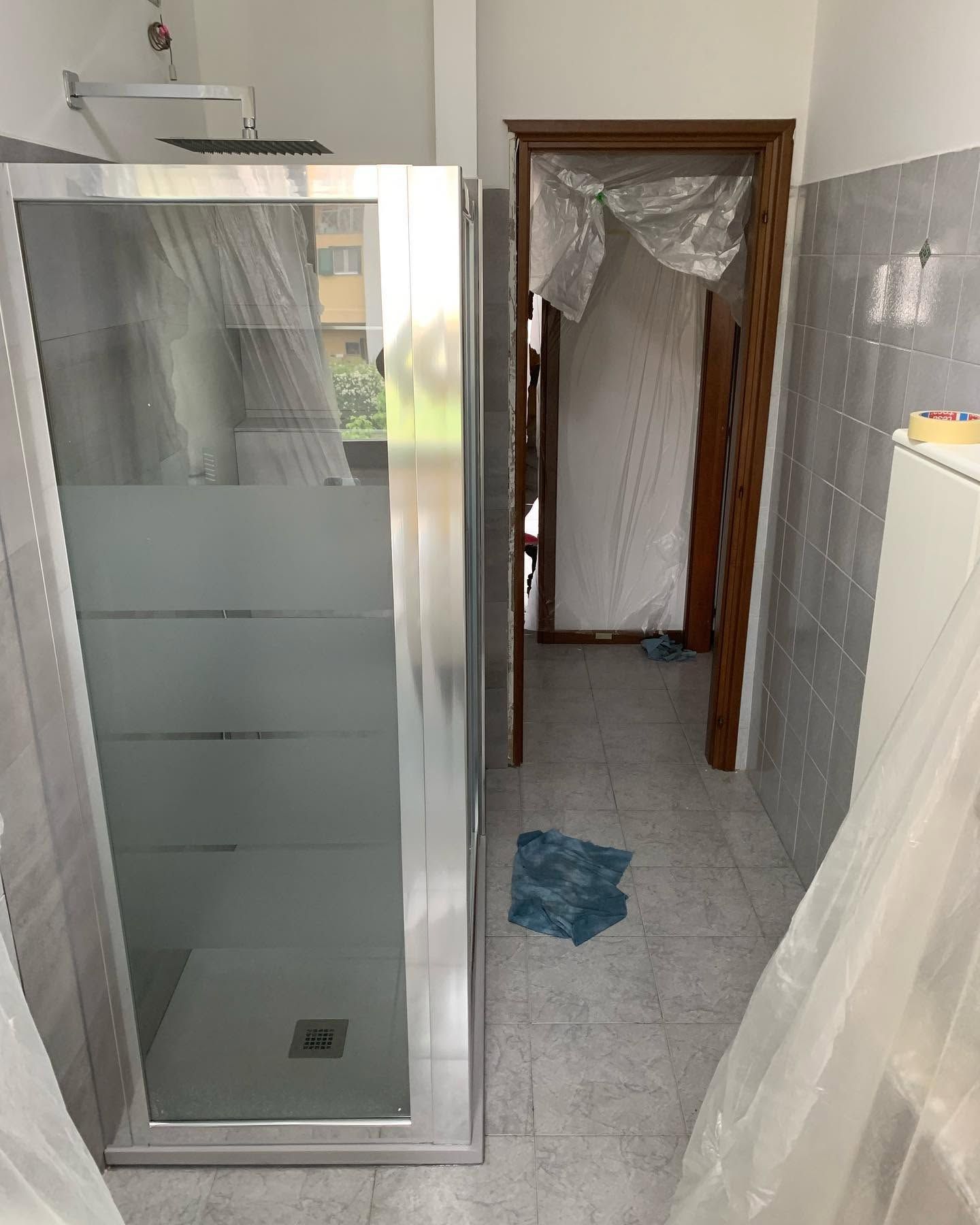 Piccolo bagno con box doccia in vetro, pareti piastrellate e porta con tenda.