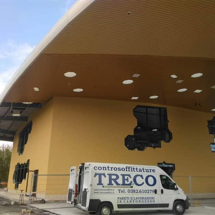 Un furgone bianco della TREC parcheggiato accanto a un edificio giallo con un grande tetto sporgente.