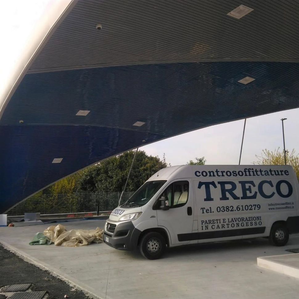Furgone bianco TRECO per traslochi parcheggiato all'aperto sotto una tettoia blu curva.