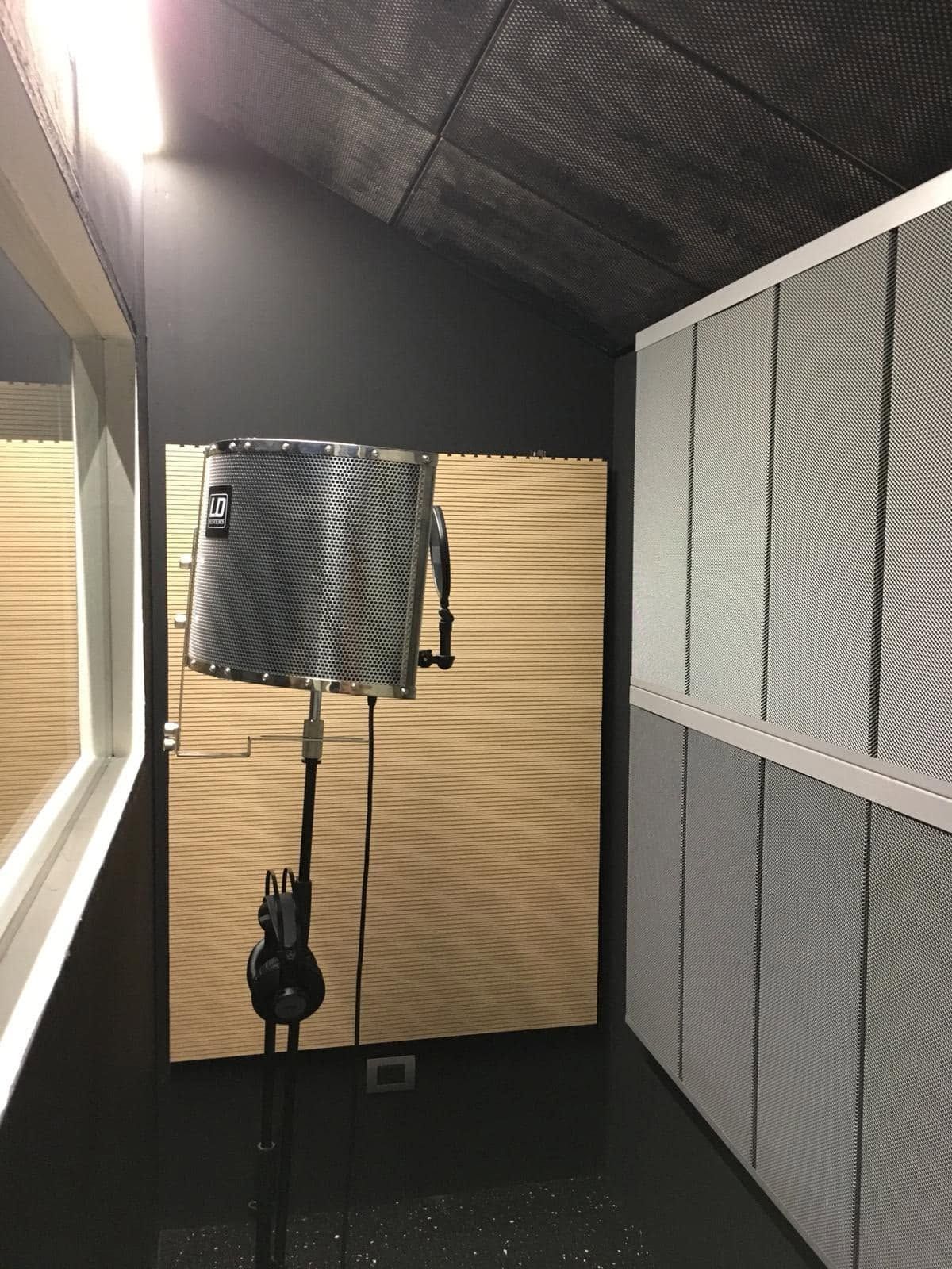Piccola cabina di registrazione con asta per microfono e pannelli fonoassorbenti alle pareti e al soffitto.