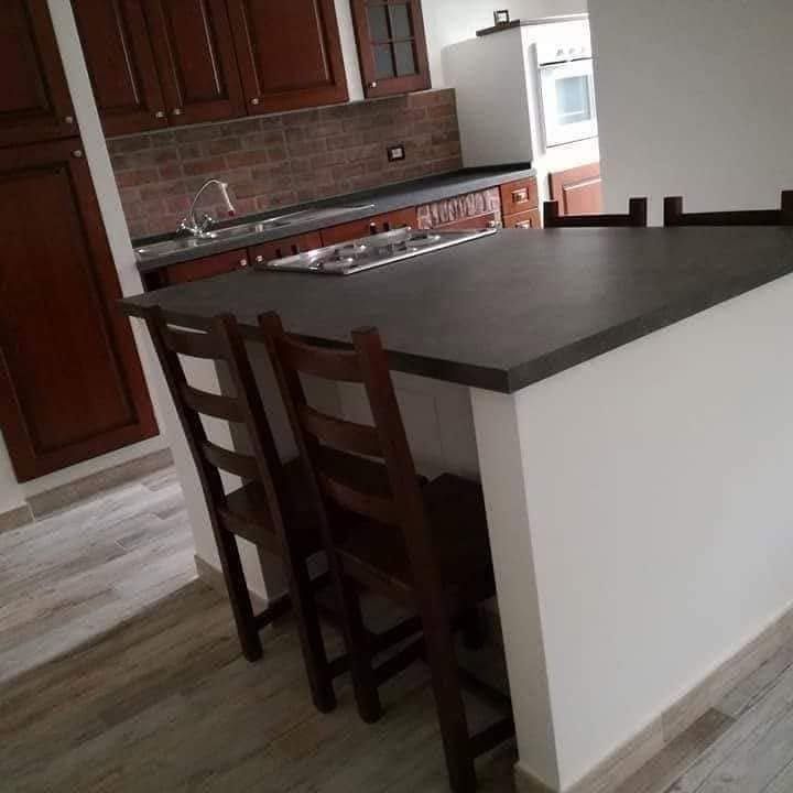 Cucina moderna con isola in legno scuro, sgabelli da bar, paraschizzi piastrellato e frigorifero bianco.