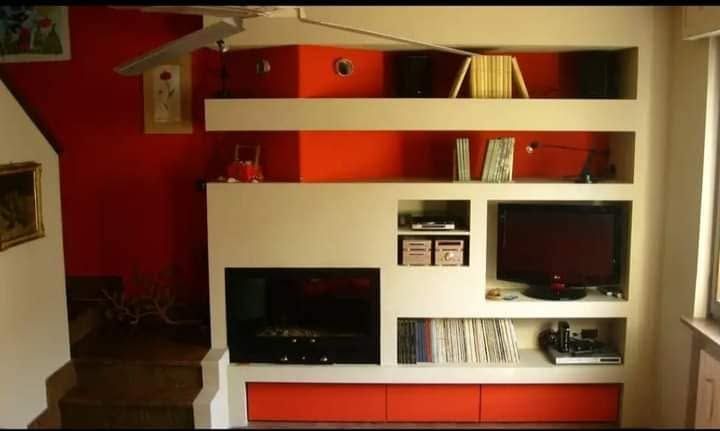 Mobile moderno con scaffalatura bianca, TV, libri e cassetti arancioni in un soggiorno con pareti rosse.