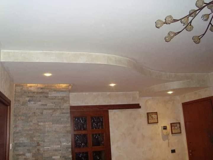 Soffitto del soggiorno con faretti a incasso, parete decorativa in pietra, porta in legno e lampadario decorativo.