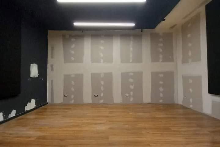 Stanza vuota e non rifinita con pavimento in legno, rattoppi di cartongesso grigio e lampade a soffitto scure.