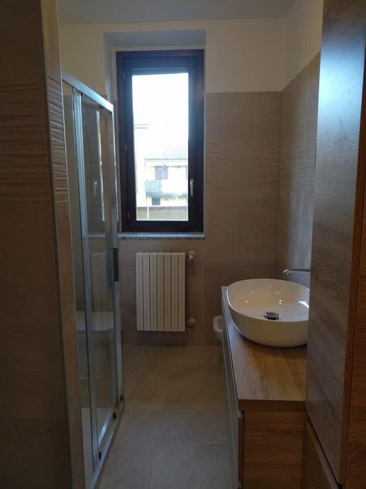 Bagno stretto con lavandino, mobiletto con specchio, termosifone e finestra in fondo.