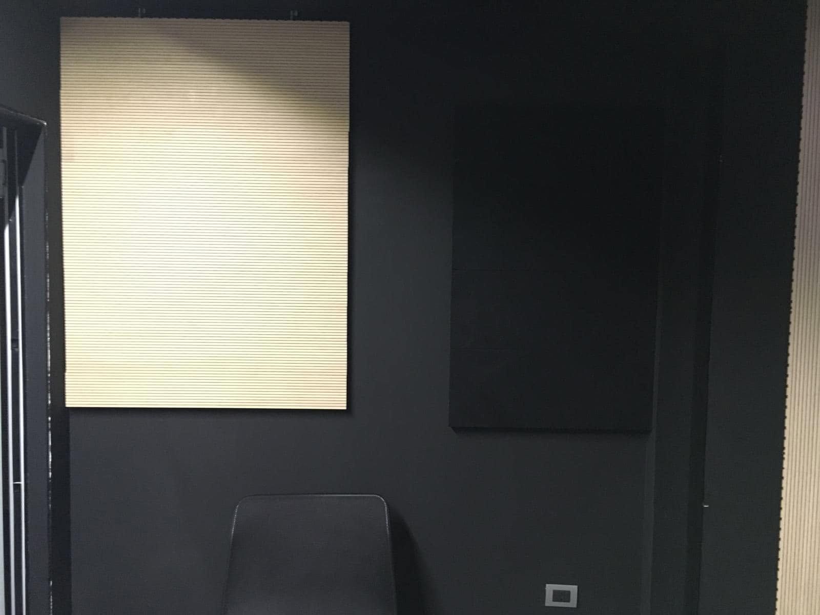 Stanza buia con un pannello rettangolare luminoso, un pannello a parete nero, una sedia e una piccola presa elettrica a muro.