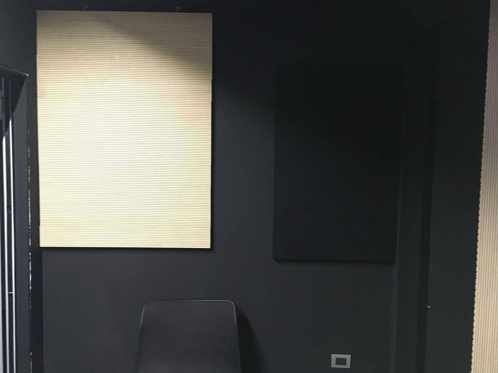 Stanza buia con un pannello rettangolare luminoso, un pannello a parete nero, una sedia e una piccola presa elettrica a muro.