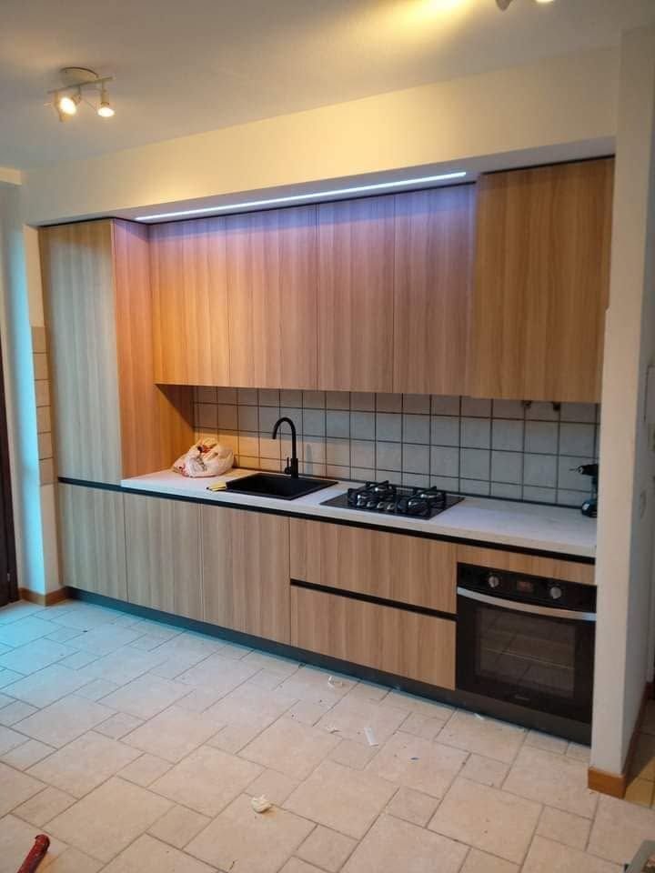 Cucina moderna con mobili in legno, pavimento in piastrelle bianche, piano di lavoro nero e forno e piano cottura a incasso.