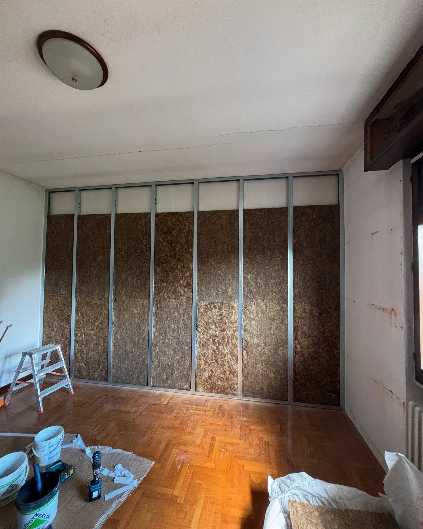 Stanza parzialmente ristrutturata con struttura a vista, pavimento in legno e attrezzi in primo piano.