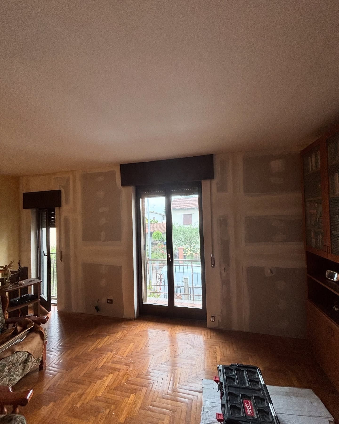 Soggiorno vuoto con pavimento in legno, bovindo e lavori di riparazione del cartongesso in corso.
