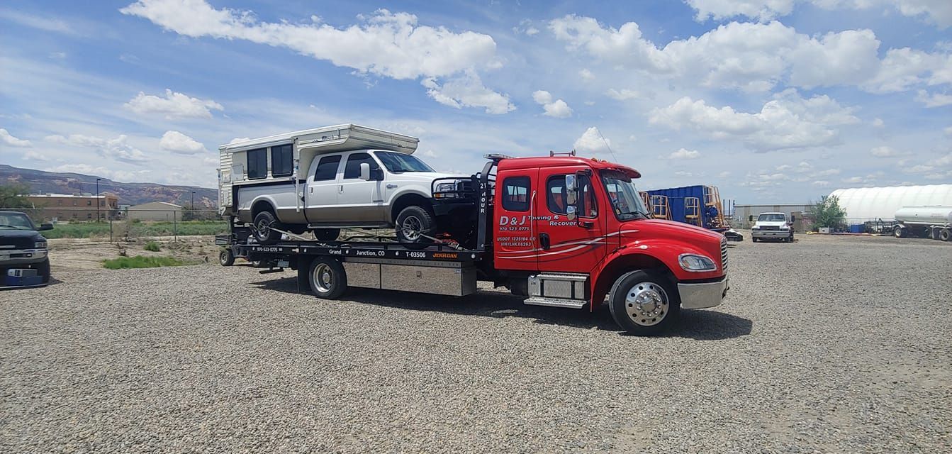Red tow truck carrying a white SUV on a gravel lot under a cloudy sky