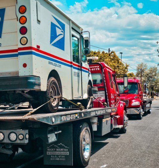 Tow trucks carrying USPS trucks lined up on a street under a blue sky