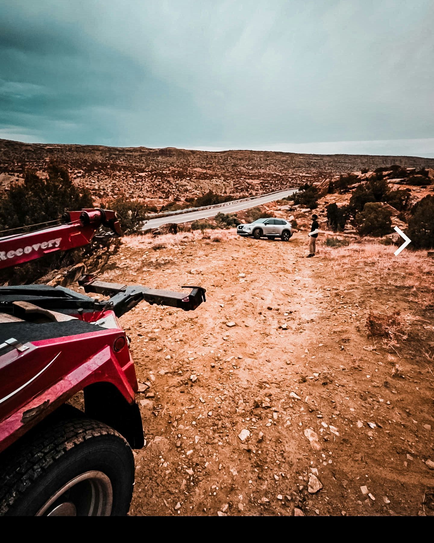 Red off-road vehicle on a rocky desert trail overlooking a white SUV in the distance.