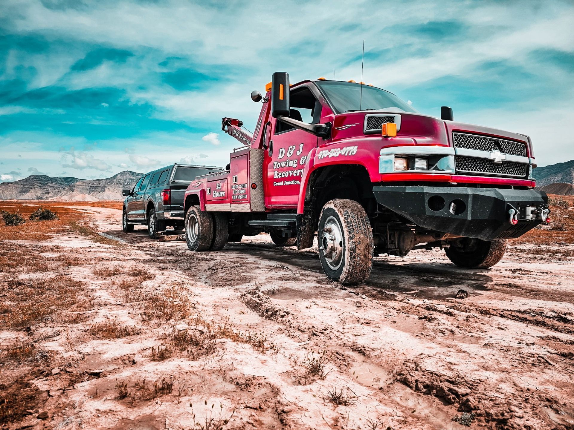 Red tow truck hauling a car across a muddy, snowy off-road landscape