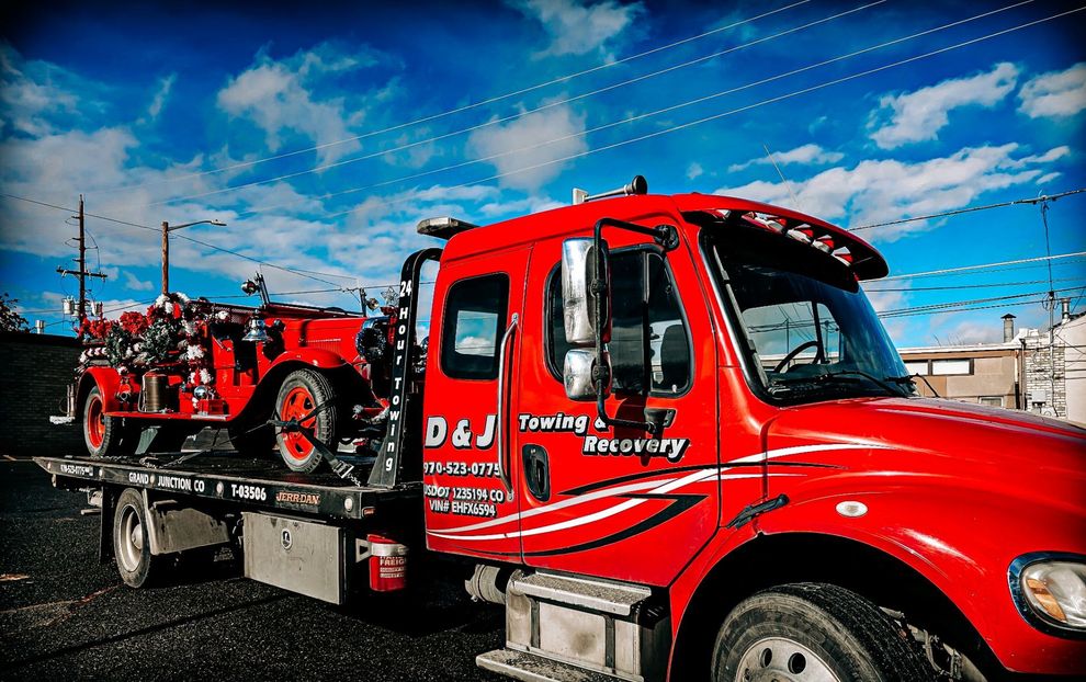 Red tow truck carrying a red off-road vehicle on a trailer under a blue sky