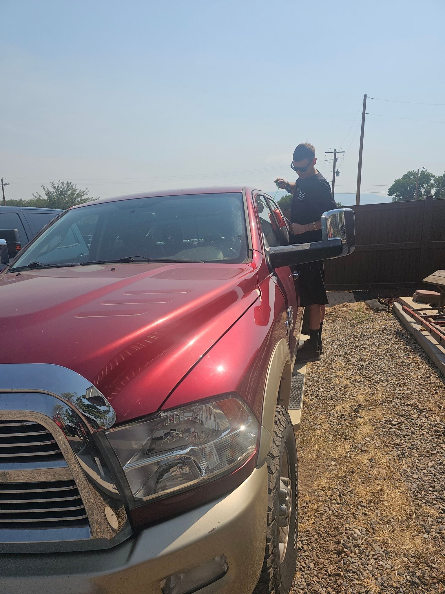 Person standing beside a red pickup truck in a gravel area under bright sunlight