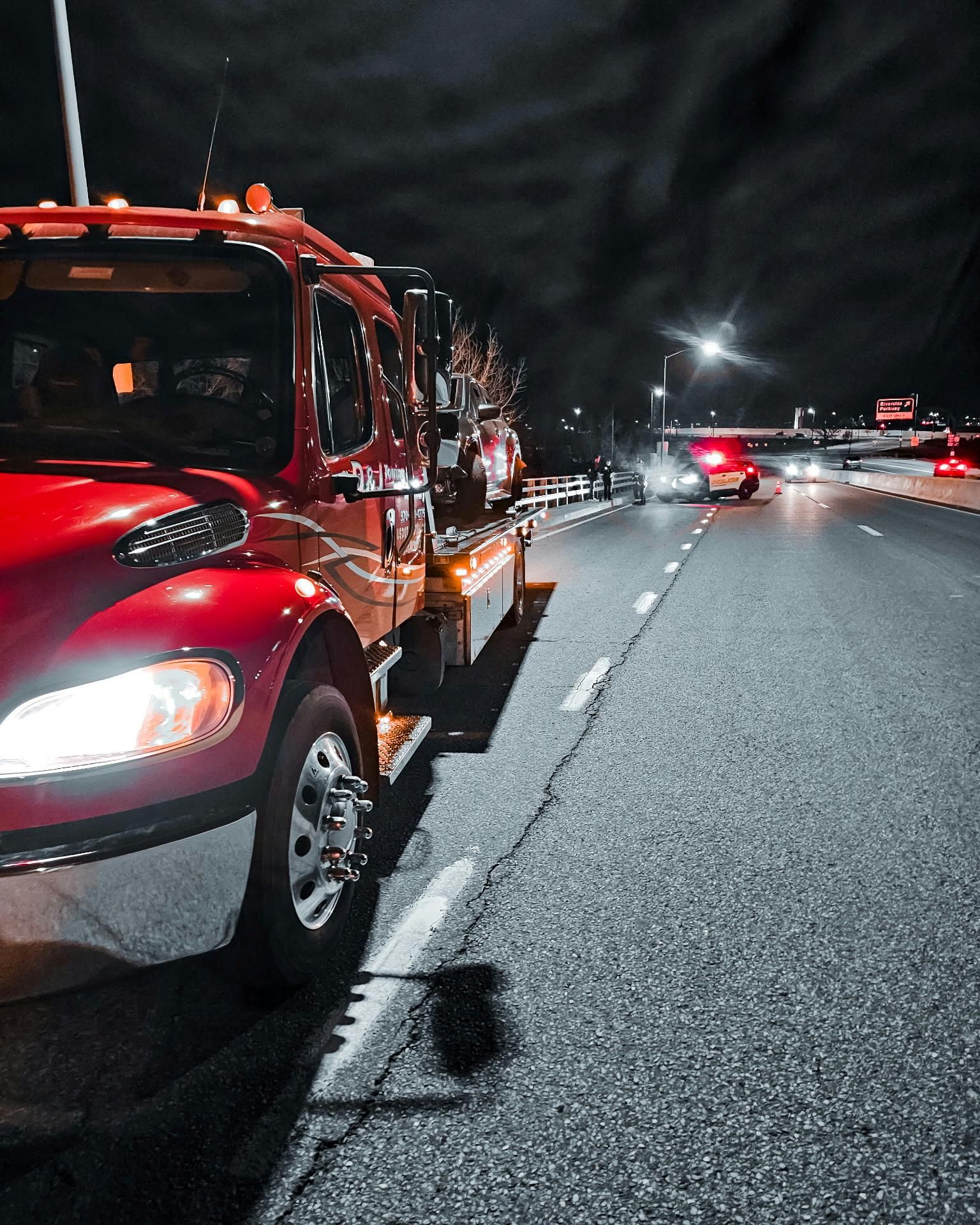 Tow truck parked on a dark highway shoulder at night with traffic ahead and road debris visible.