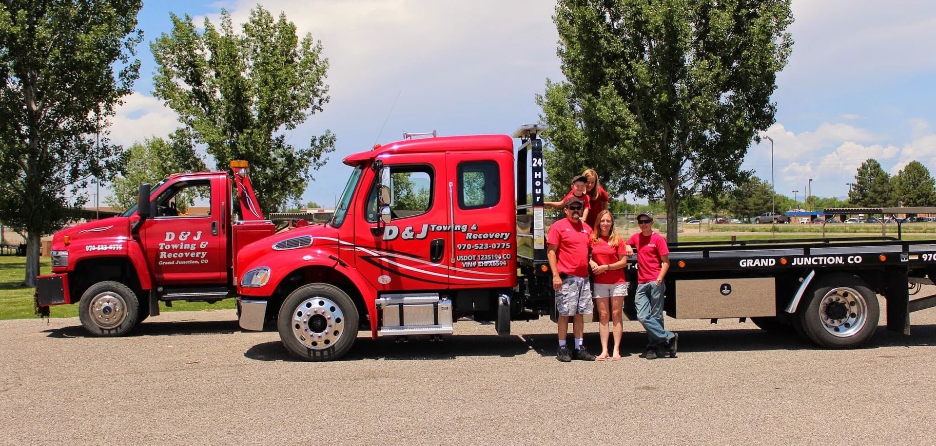 Red tow truck and flatbed truck with three people standing beside them in a parking lot.