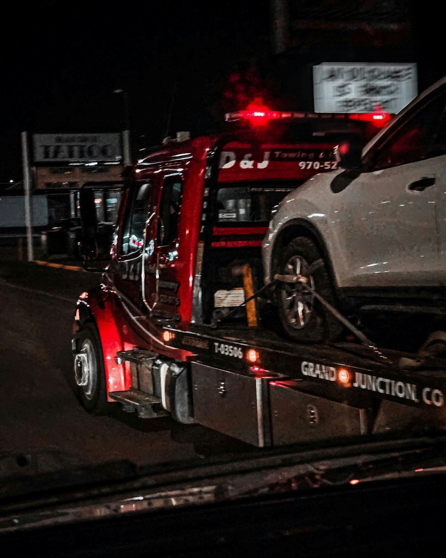 Tow truck hauling a white SUV at night, with red emergency lights flashing.