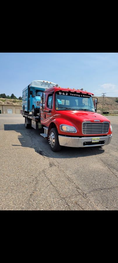 Red tow truck with blue equipment parked on cracked asphalt under a clear sky.
