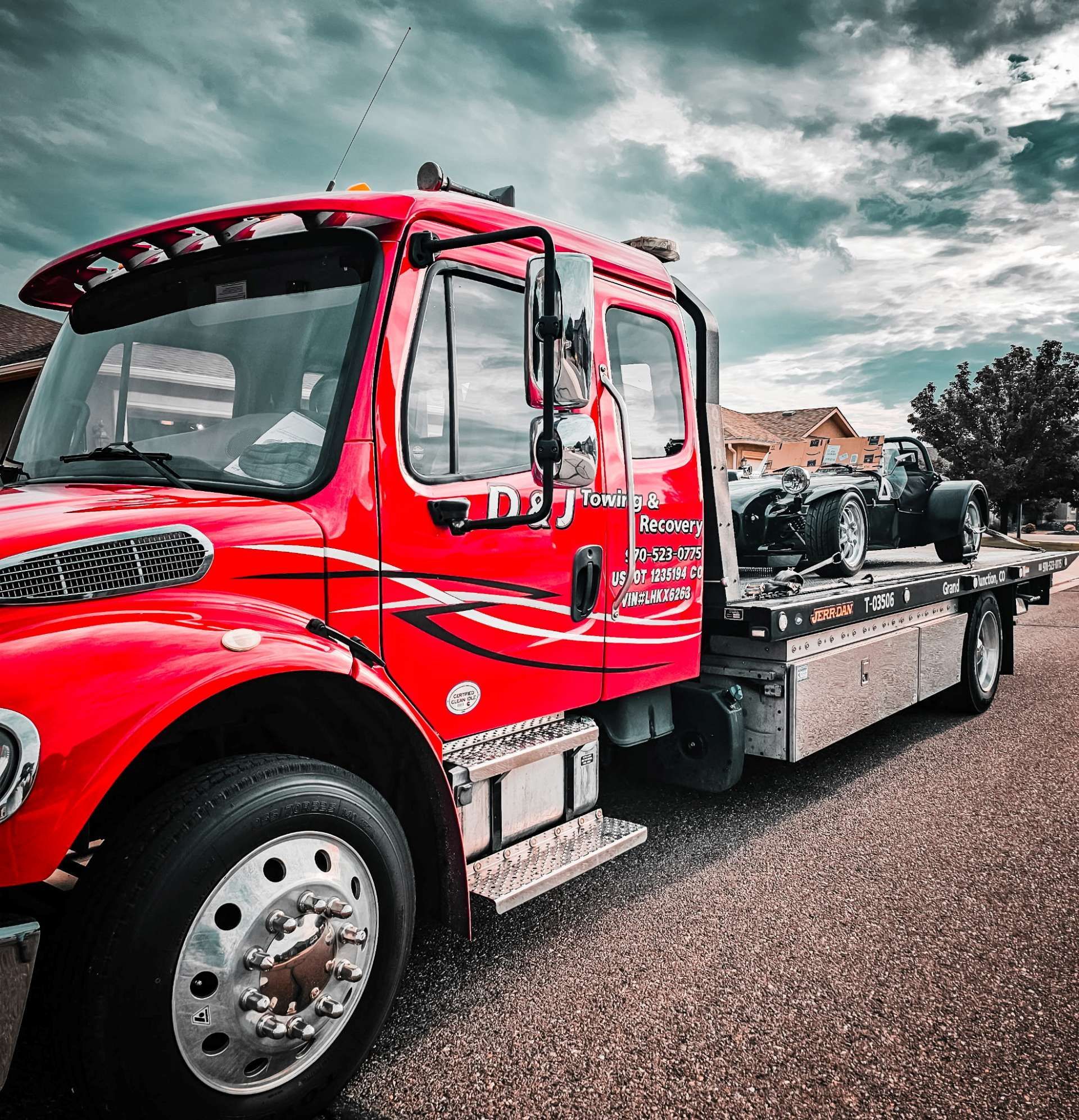 Red tow truck with flatbed parked on a road under cloudy skies