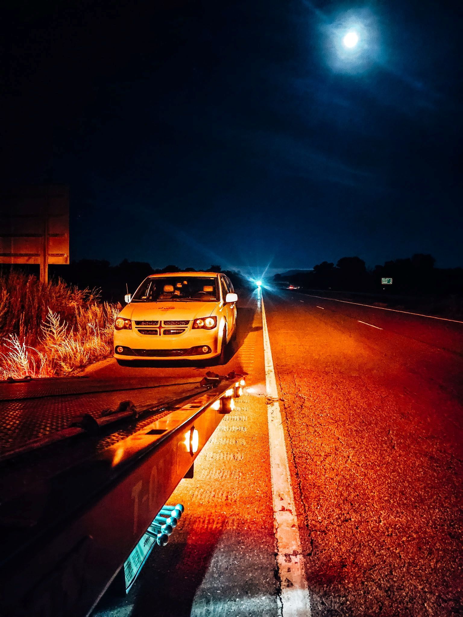 Parked white car on a dark roadside at night, lit by orange streetlights under a bright moon