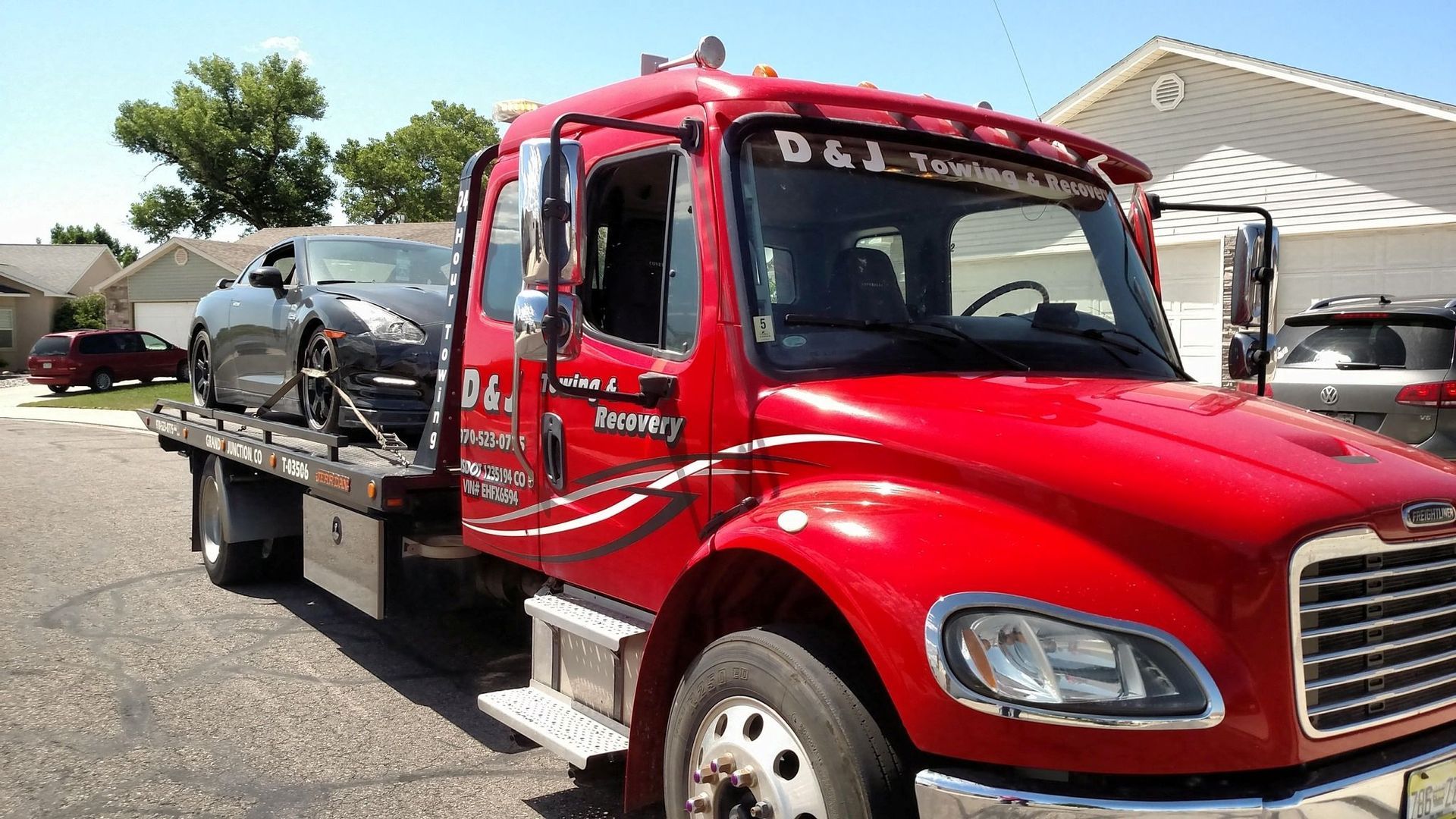 Red tow truck hauling a damaged black car on a flatbed in a parking lot
