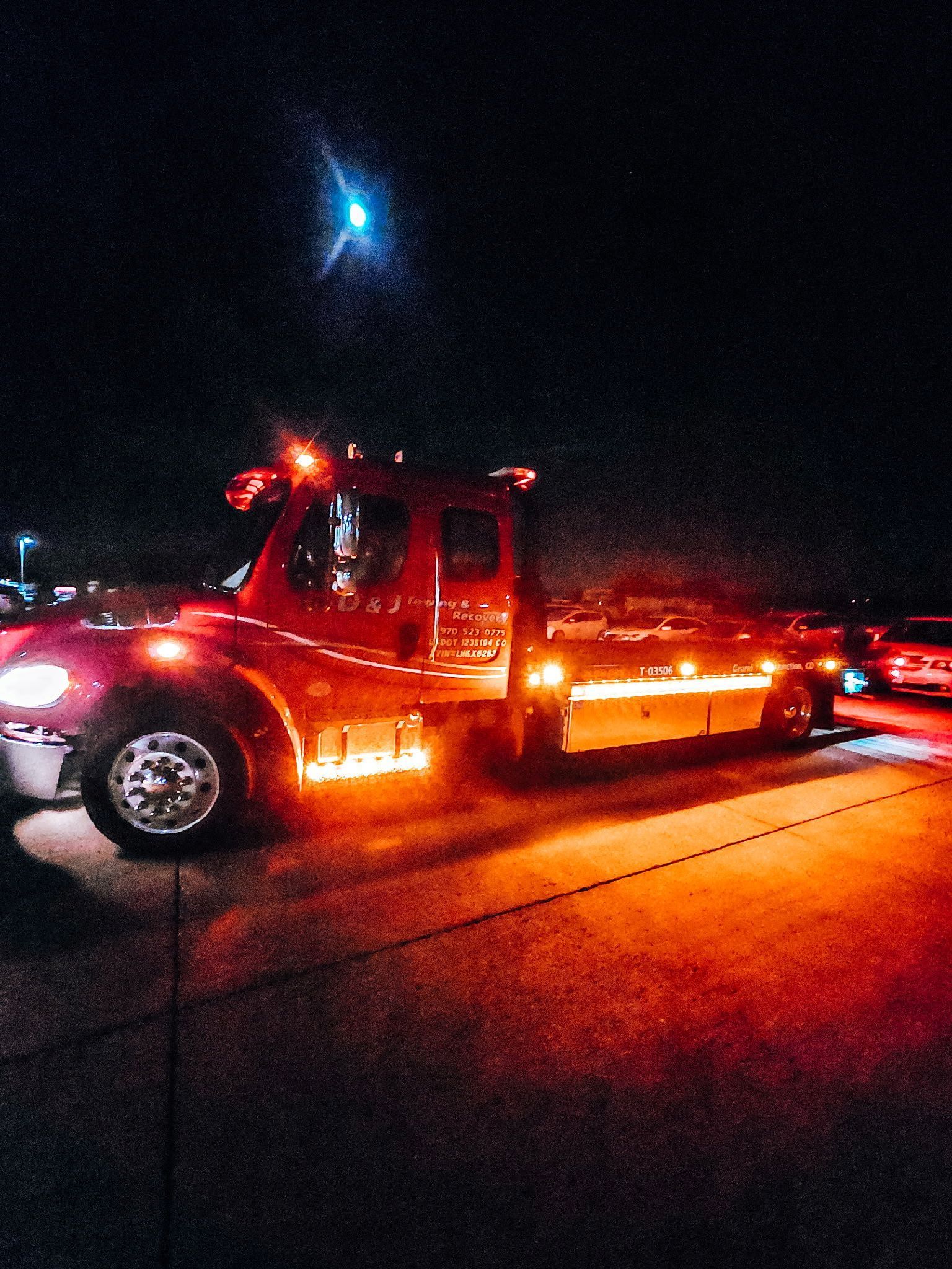 Red tow truck with bright orange lights parked on a dark street at night