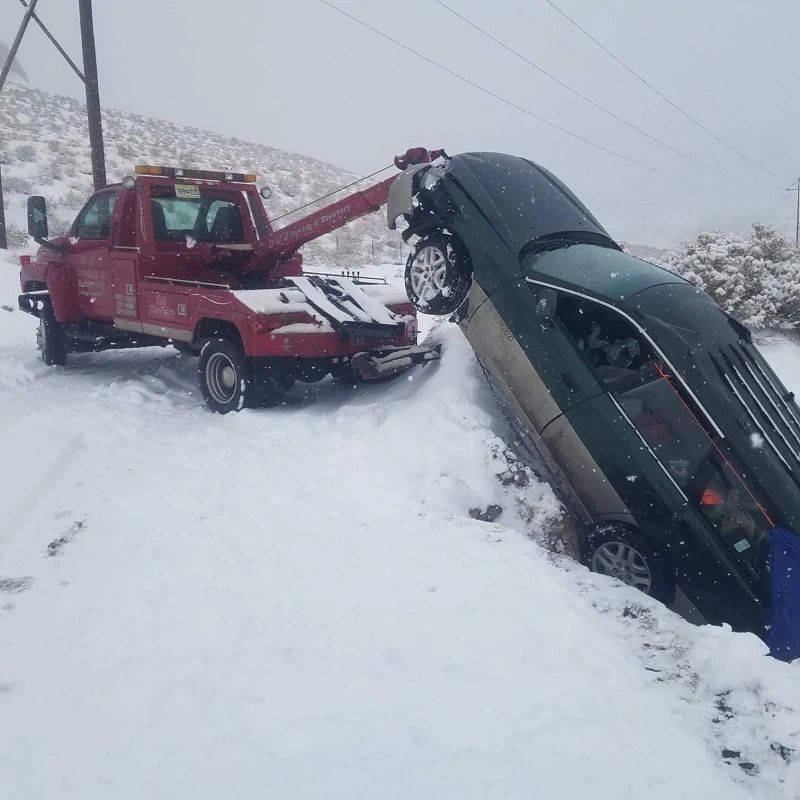 Red tow truck pulling a black car from a snowbank on a snowy roadside