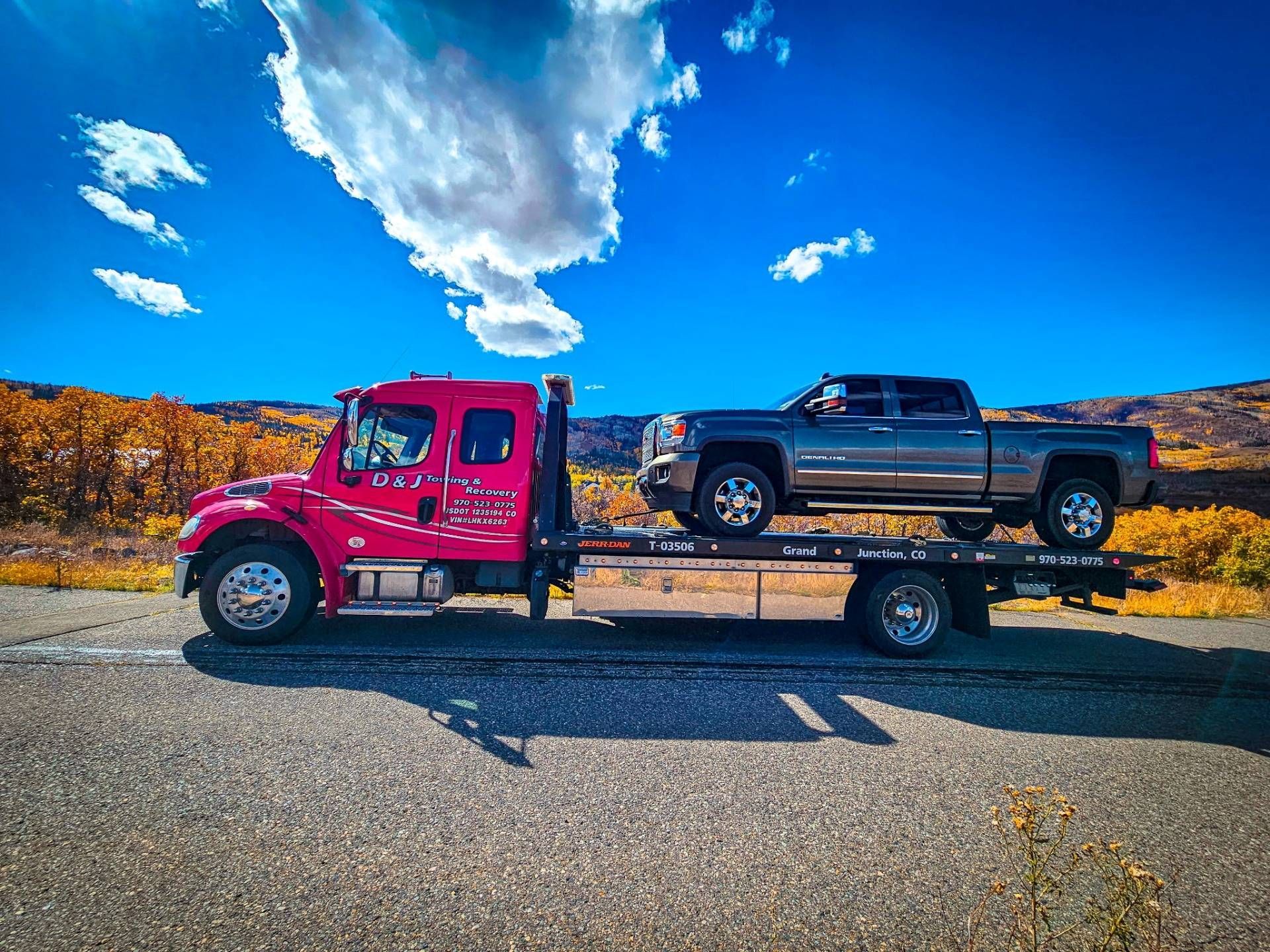 Pink tow truck hauling a black pickup on a trailer under a bright blue sky