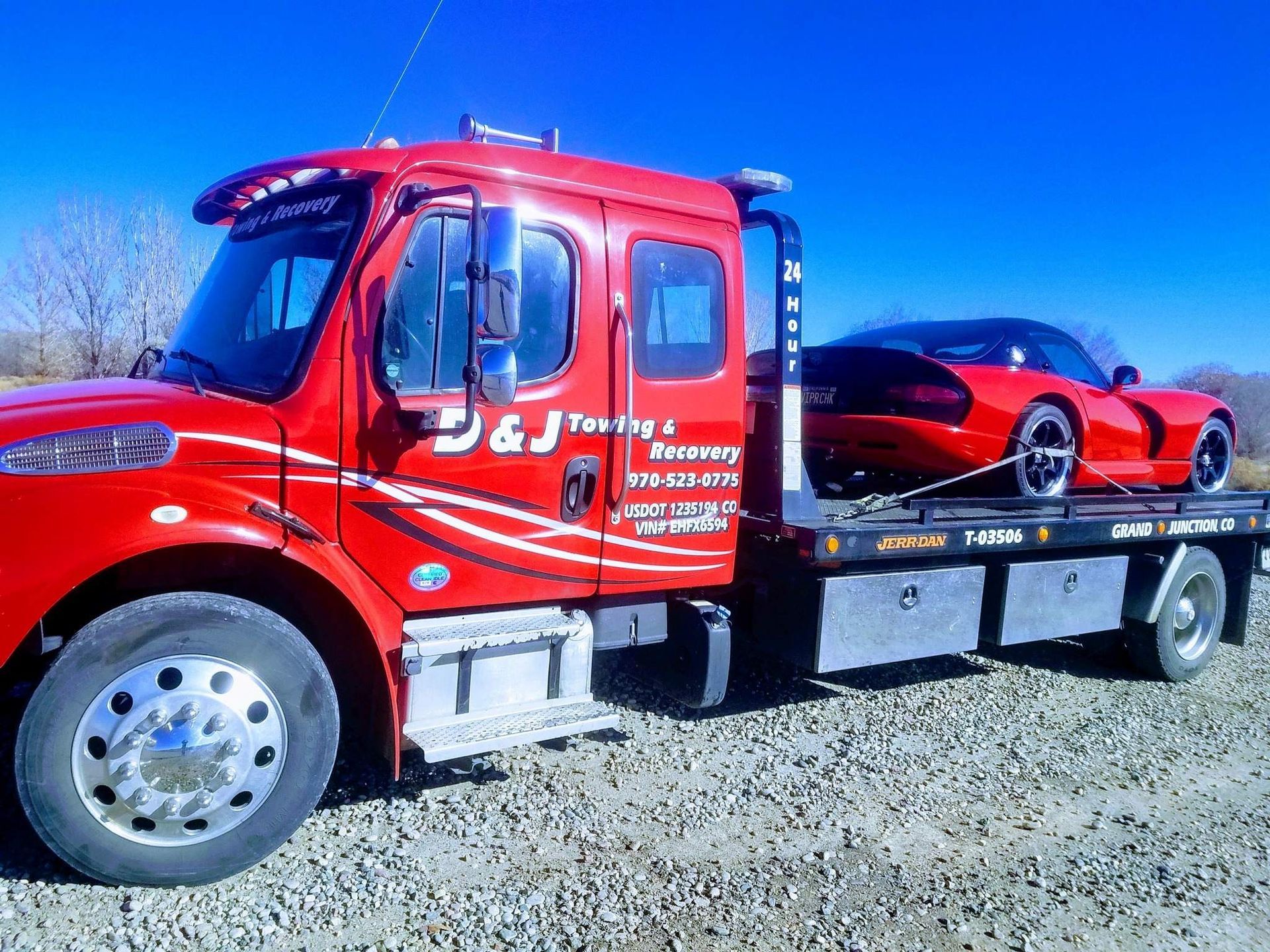 Red tow truck carrying a red sports car on a flatbed trailer under a bright blue sky