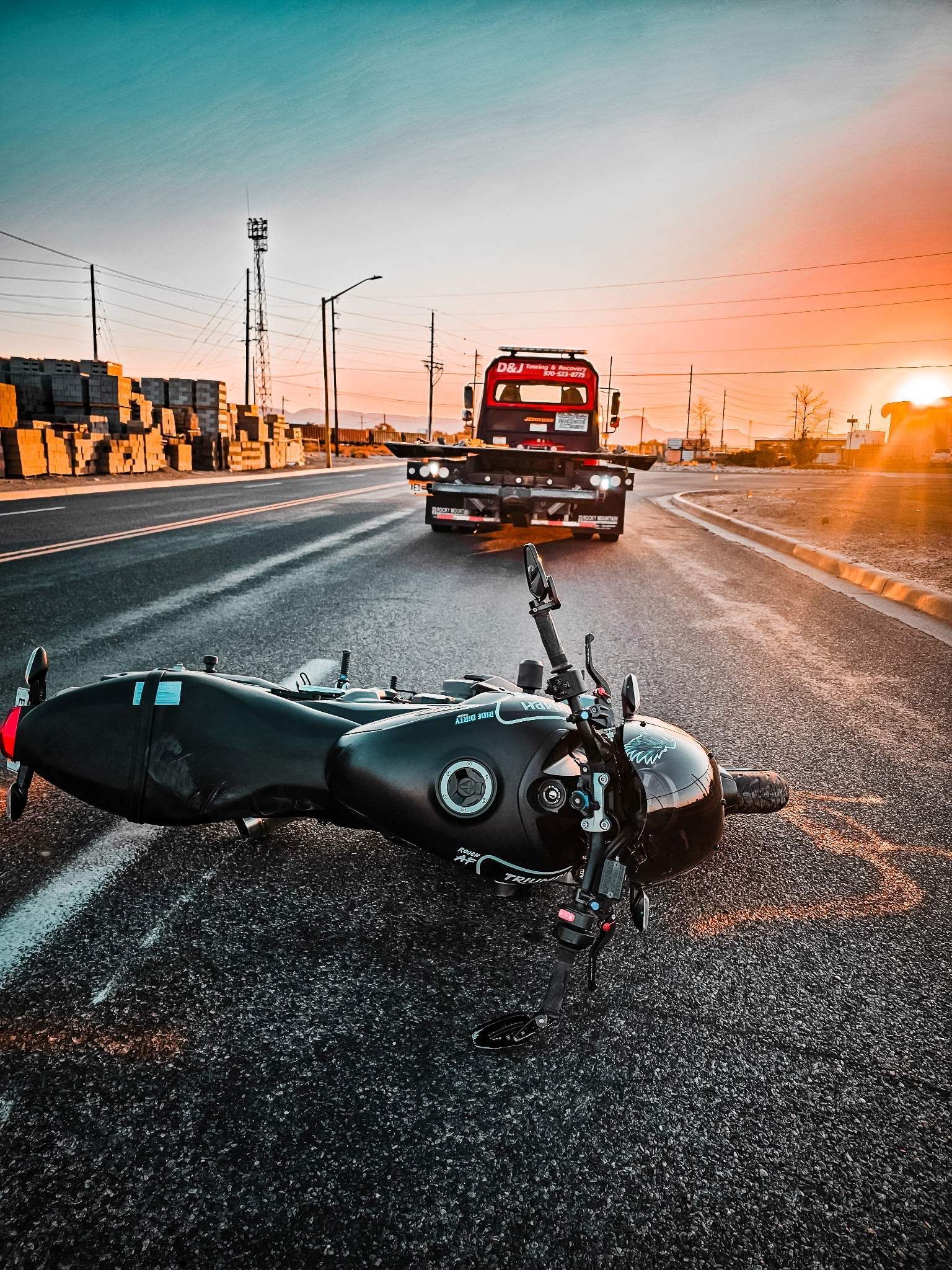 Motorcycle lying on wet road behind a pickup truck at sunset, with debris scattered across the lane.